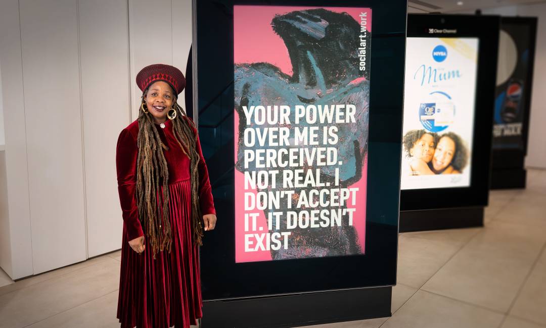 Ngozi Fulani, CEO Sistah Space, stands in front of a digital screen displaying her quote and artwork by Martin Firrell, at Clear Channel's HQ in London