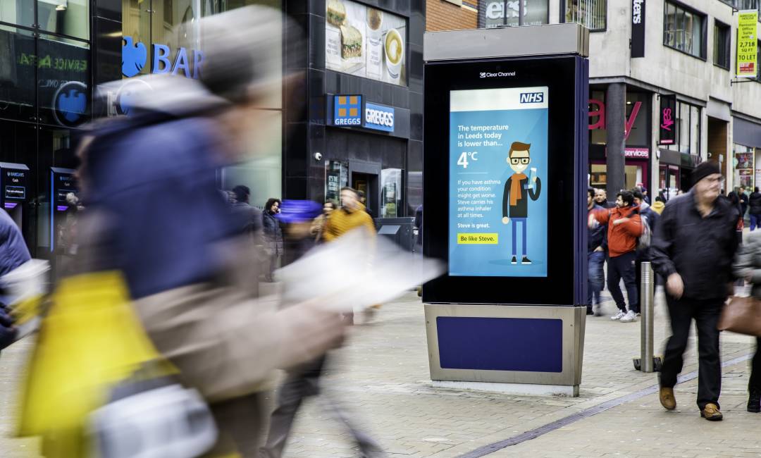 Clear Channel Adshel Live screen showing NHS temperature-triggered digital advertising campaign on a busy high street