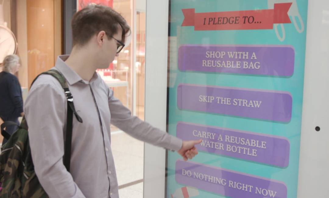 Man in shopping mall using digital screen showing Dumb Ways to Kill Oceans interactive campaign