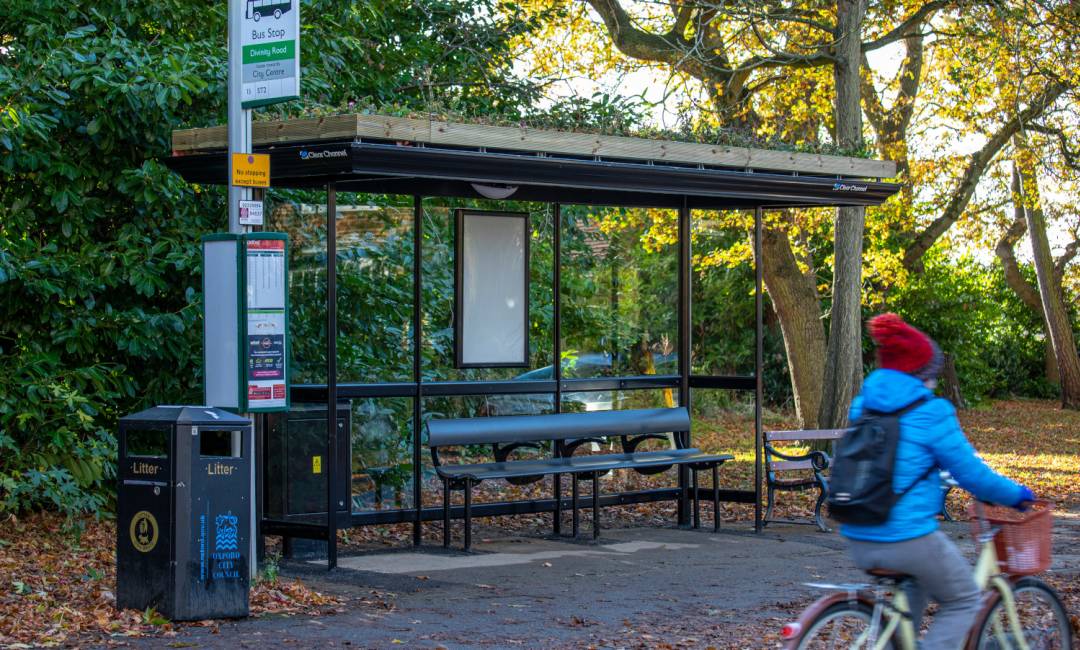 A bus shelter with a living roof in Oxford, located near a park and with a cyclist going past