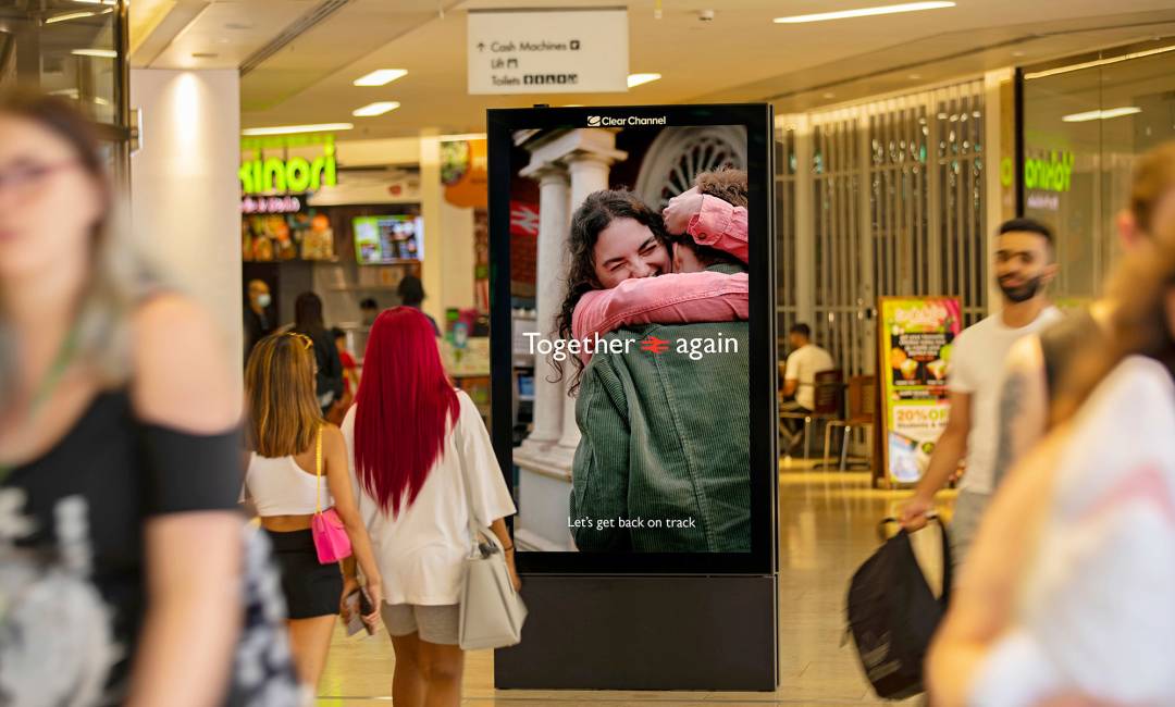 Digital poster in a shopping mall showing two people hugging with the text 'together again' overlaid