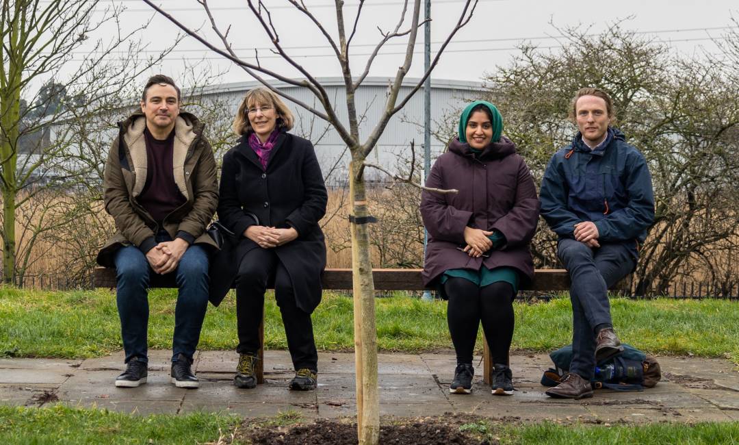 Four people sitting on a bench next to a newly planted tree funded by Clear Channel's re-greening and rejuvenation project