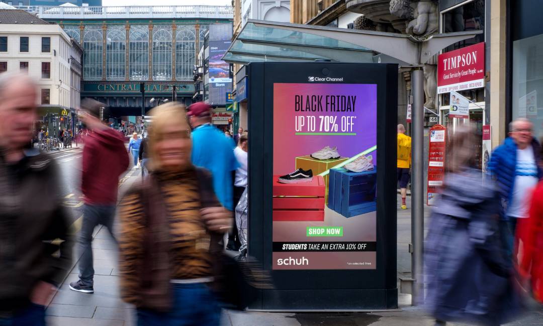 Schuh Black Friday advertisement on Adshel Live at a bus shelter on a busy road