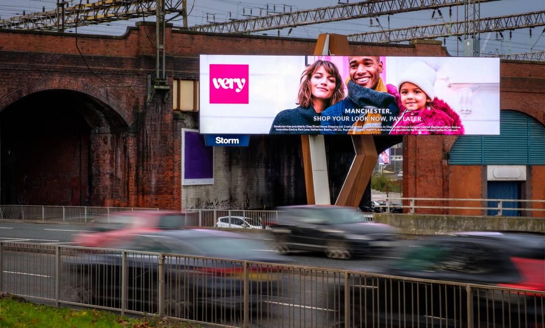 Billboard over busy road, beside train arch, displaying a fashion brand