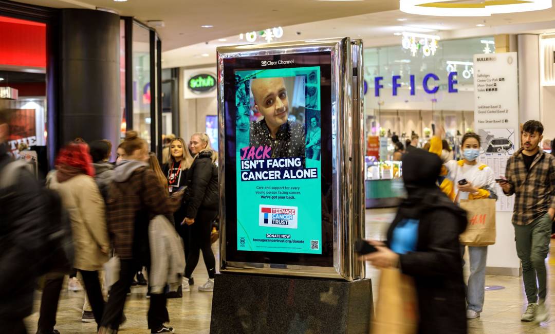 Digital screen in a busy shopping mall showing Teenage Cancer Trust ad