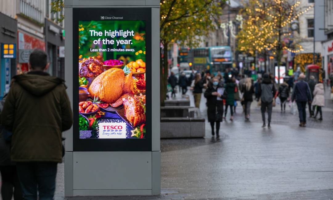 Digital screen on a busy high street showing Tesco Christmas advert