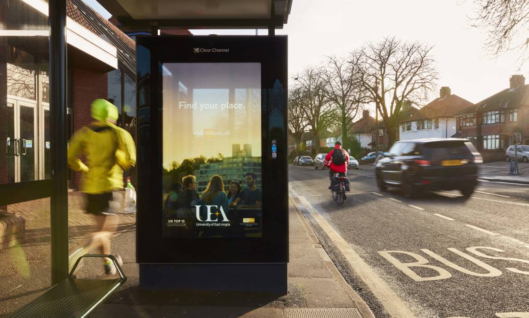 UEA's Bus Shelter ad as people run and cycle past