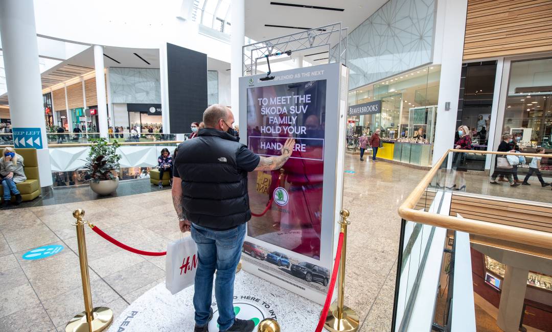 Man using digital screen in a shopping mall showing interactive Skoda advert