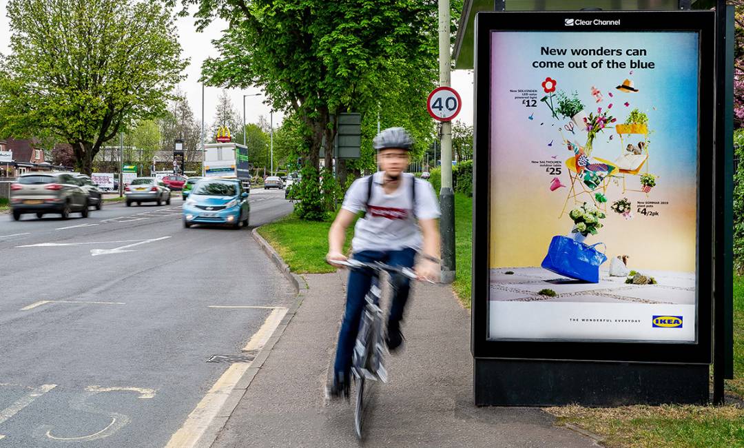 A six-sheet poster on a bus shelter with a cyclist going past