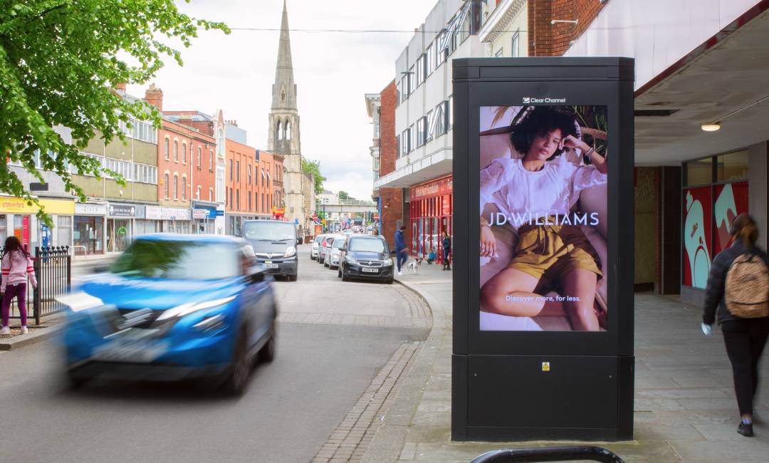 JD Williams ad on high street digital screen with cars driving past