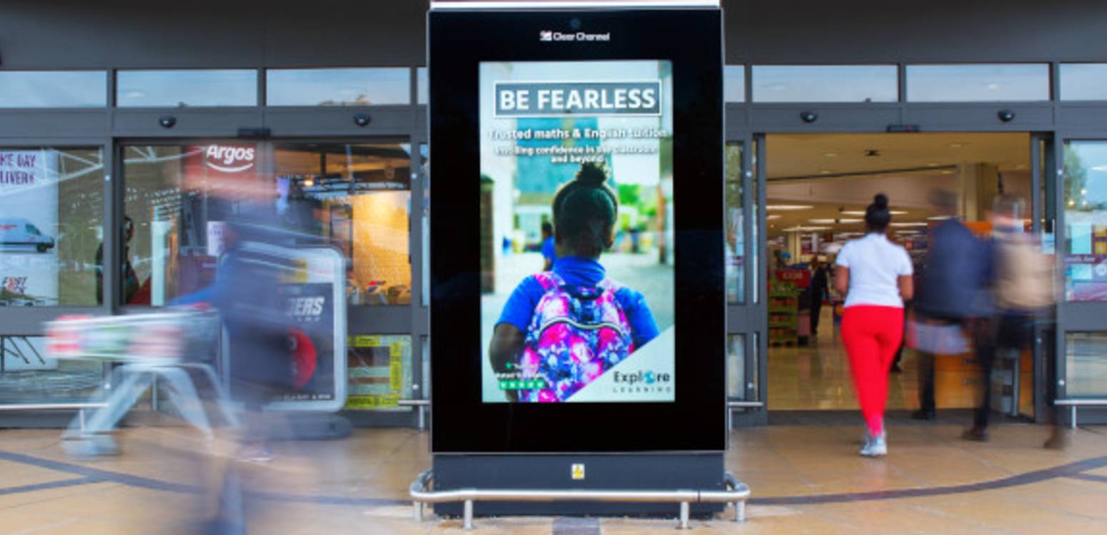 Explore Learning ad on digital screen outside Sainsbury's with people walking past