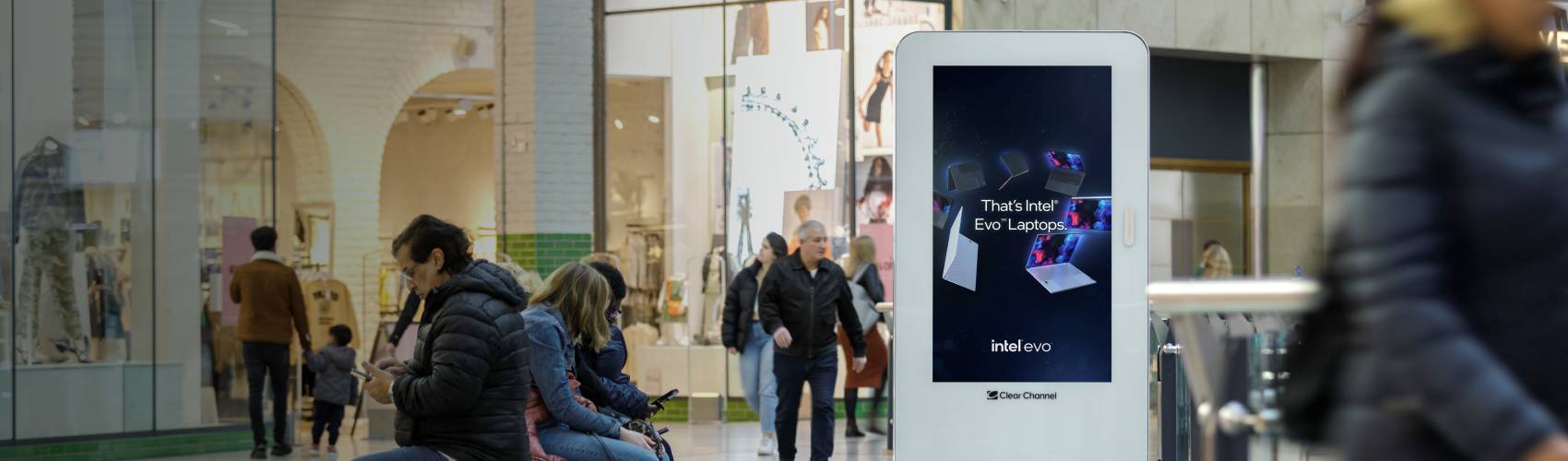 people sitting on phones in a shopping centre near a screen showing an Intel Evo advert