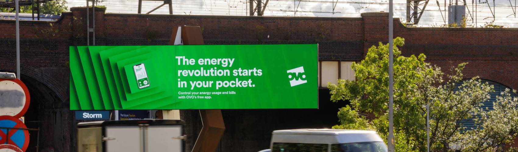 A large green digital billboard displaying an OVO campaign in Manchester