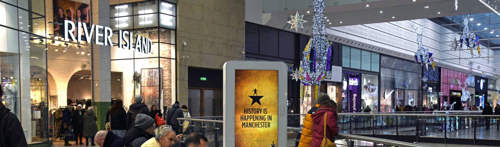 A digital screen inside a shopping mall displaying a Hamilton theatre advert