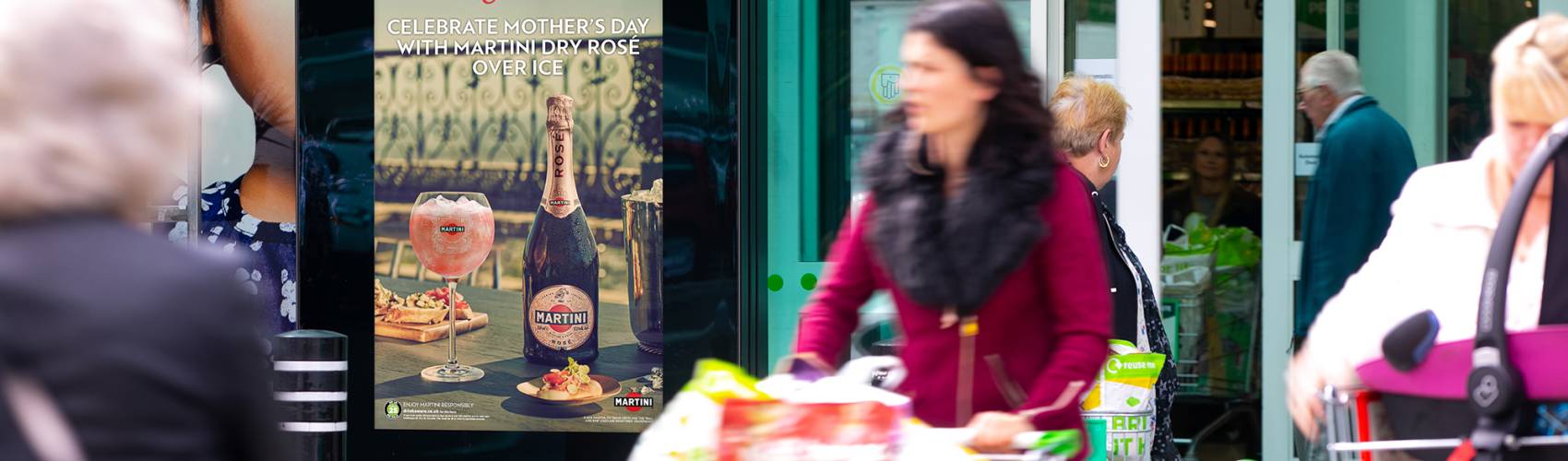 Martini advert on digital screen outside Asda with people walking past