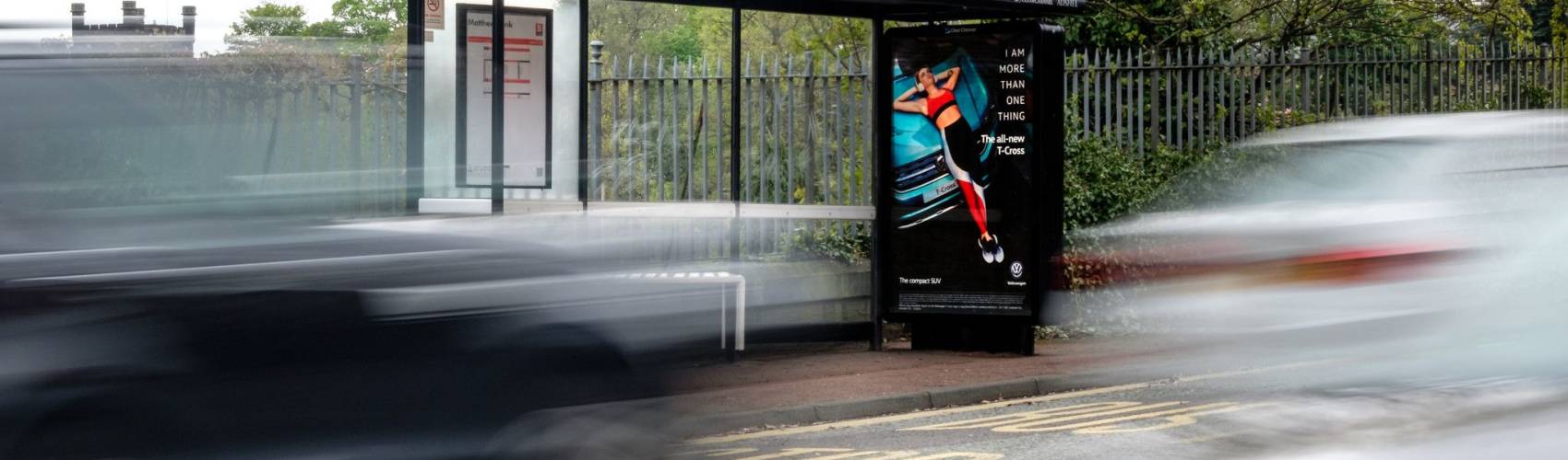 Bus stop posters featuring a woman lying on the front of car, with two cars driving past