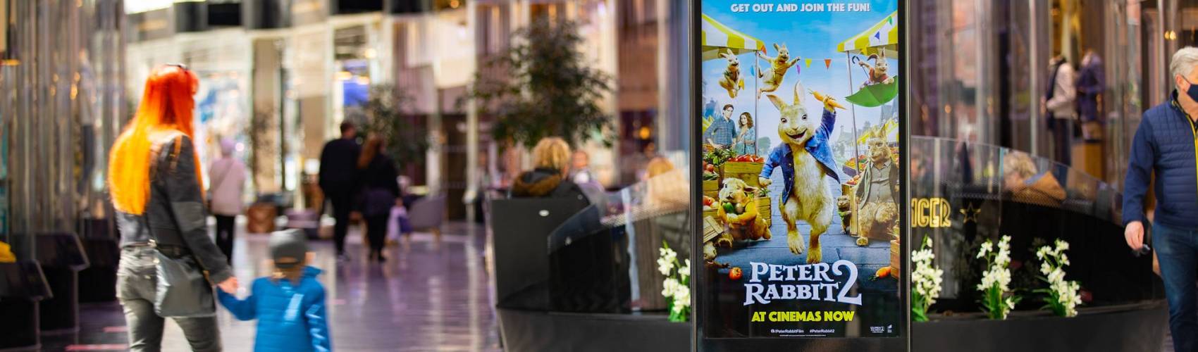 Digital screen in a busy shopping mall showing Peter Rabbit 2 ad