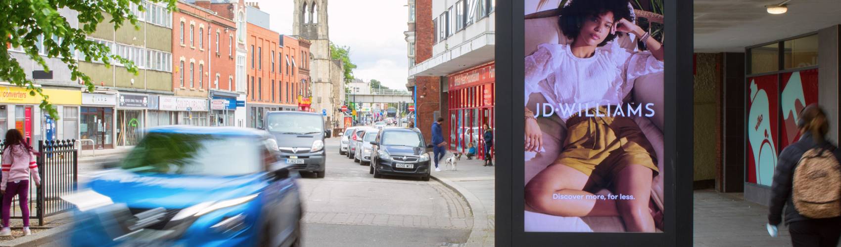 JD Williams ad on high street digital screen with cars driving past