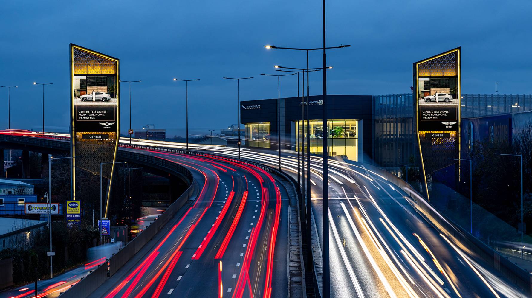 Car advert on large format digital billboard towers next to motorway at night
