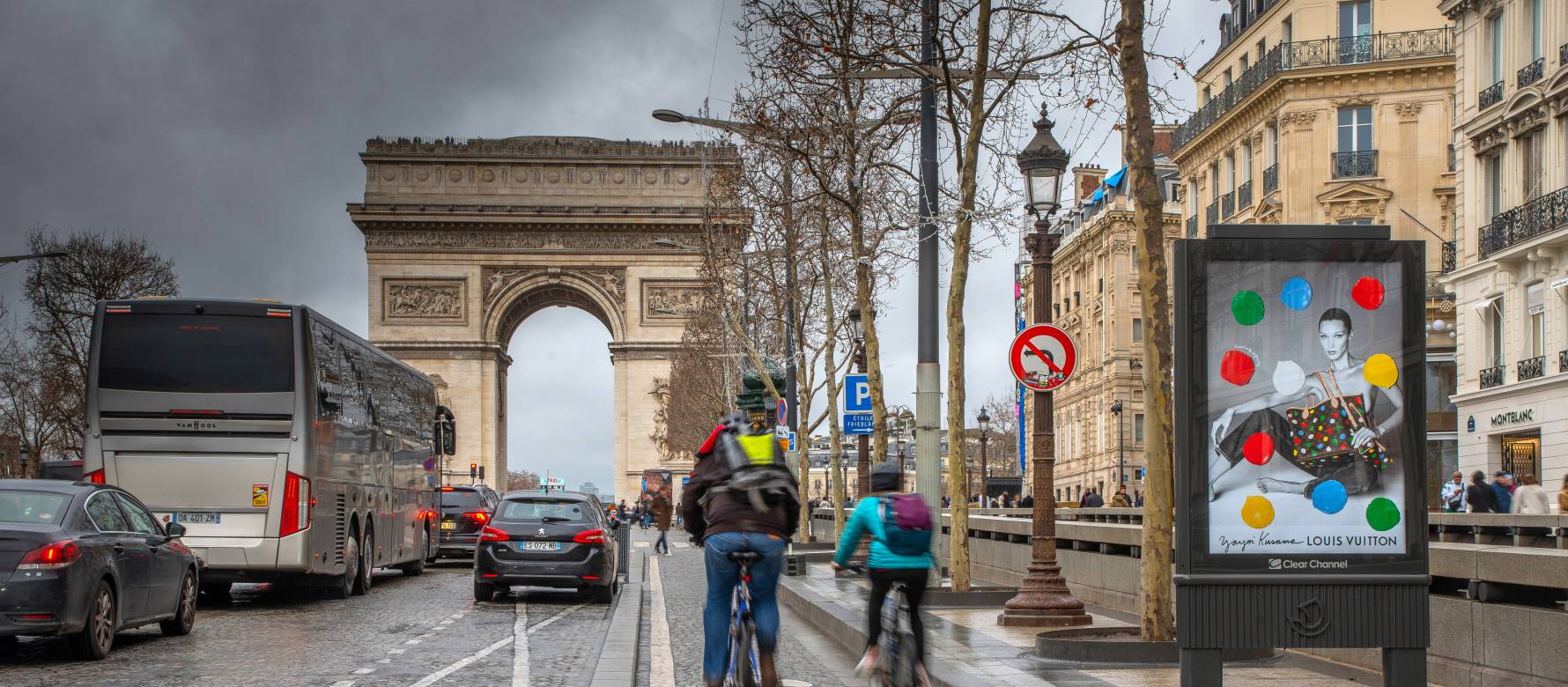 A Louis Vuitton advertisement showcased on a Clear Channel display in front of the Arc De Triomphe in Paris as pedestrians and cars pass on a rainy day