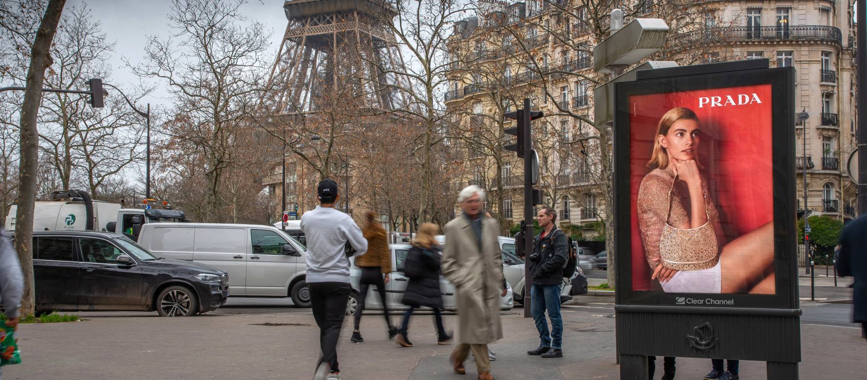 People walking by a Prada advertisement on a Clear Channel digital screen during the day, with the Eiffel Tower in the background