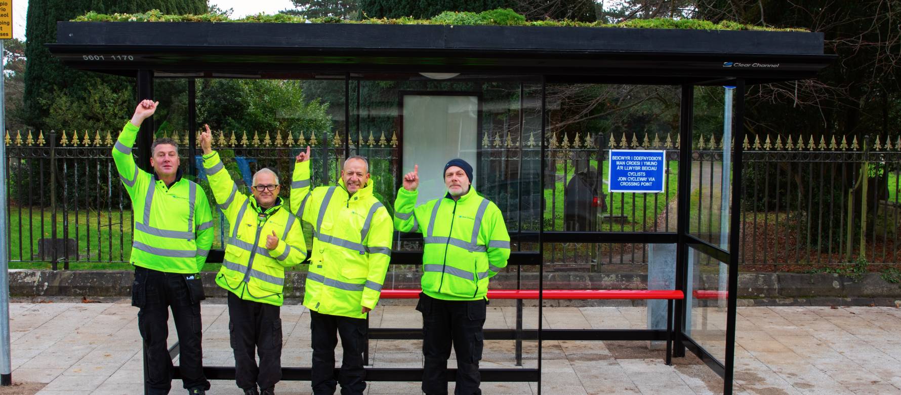 A group of men in reflective jackets standing in front of a  living roof bus stop.