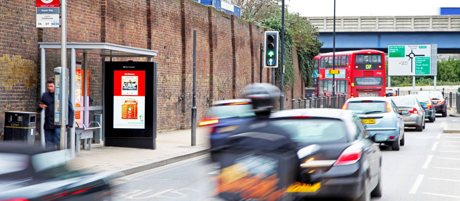 Adshel Live screen on bus stop on a busy road showing Camelot Lottery advert