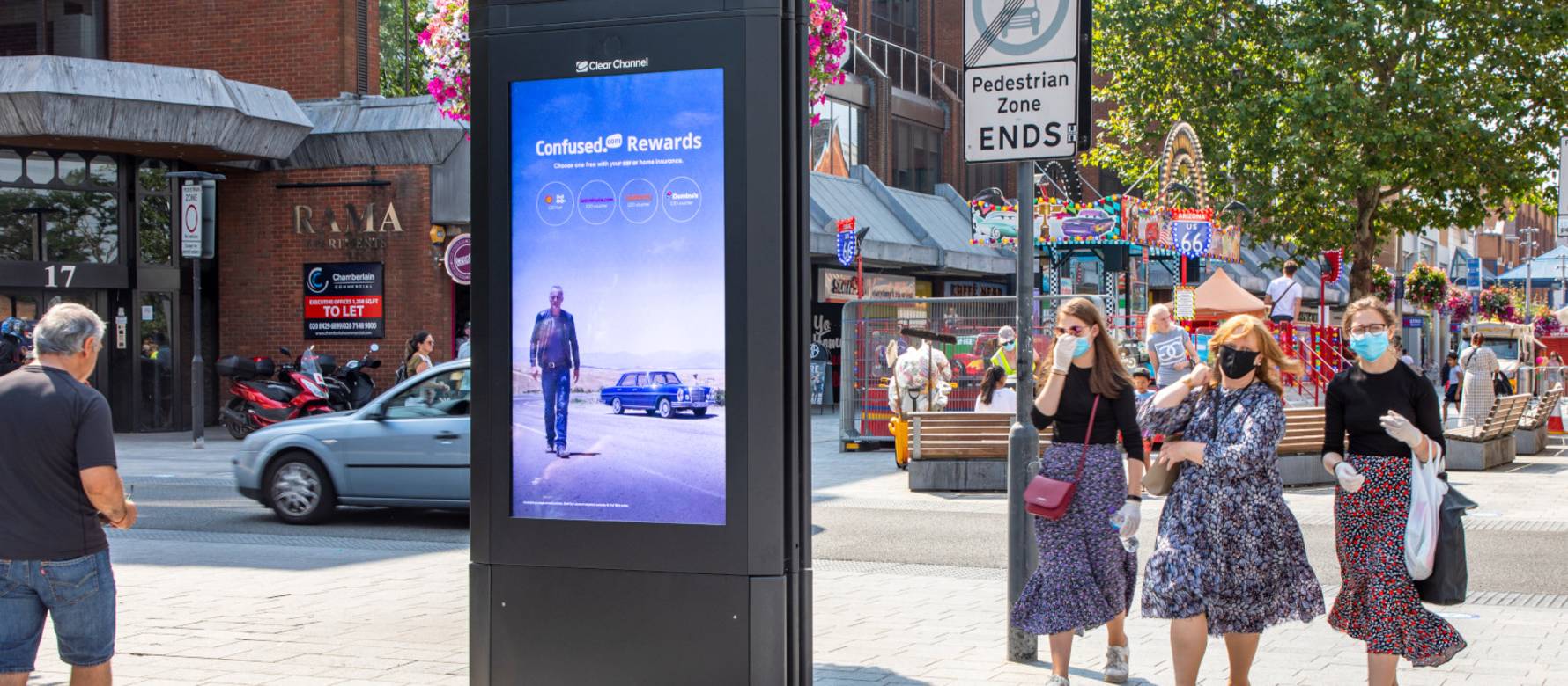 People walking past an Adshel Live display in the middle of a busy square during the day