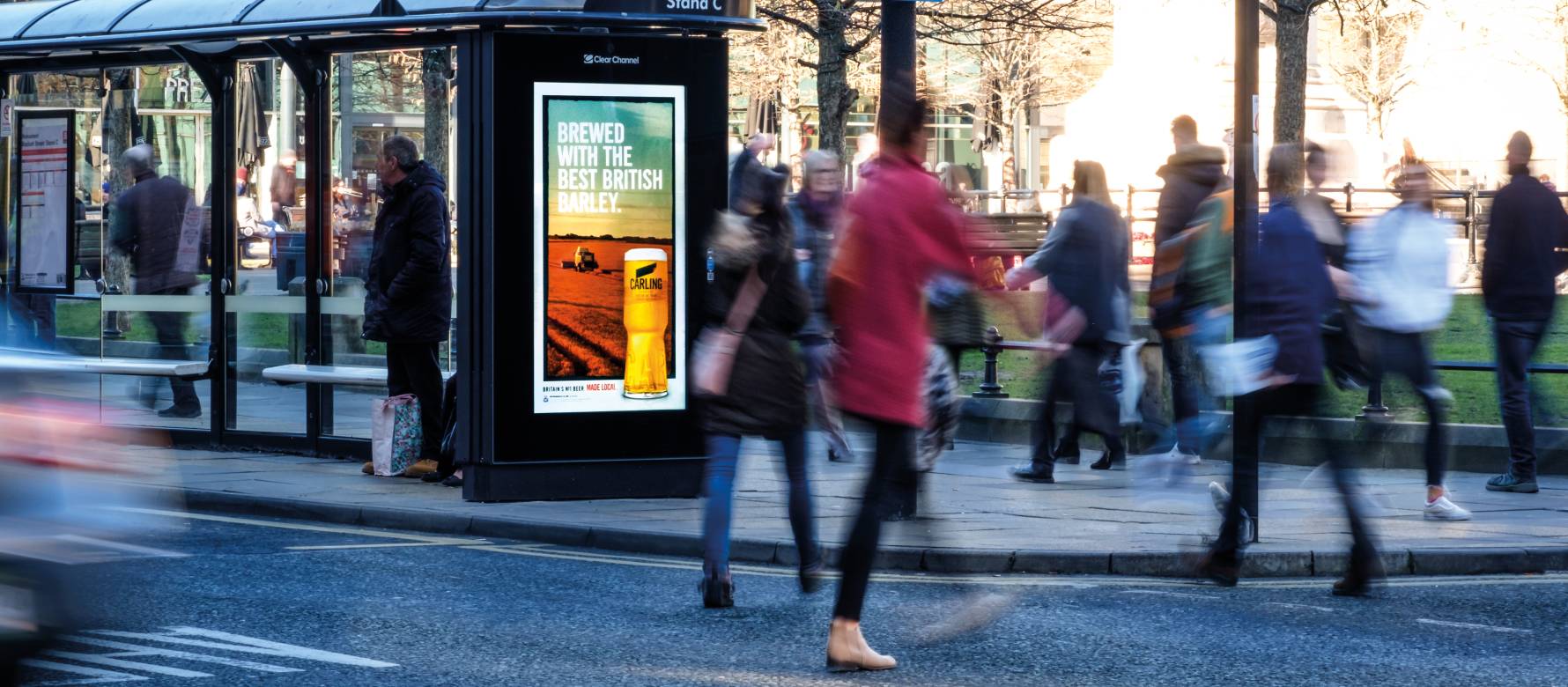 Digital screen on a bus stop of a busy road showing Carling advert.
