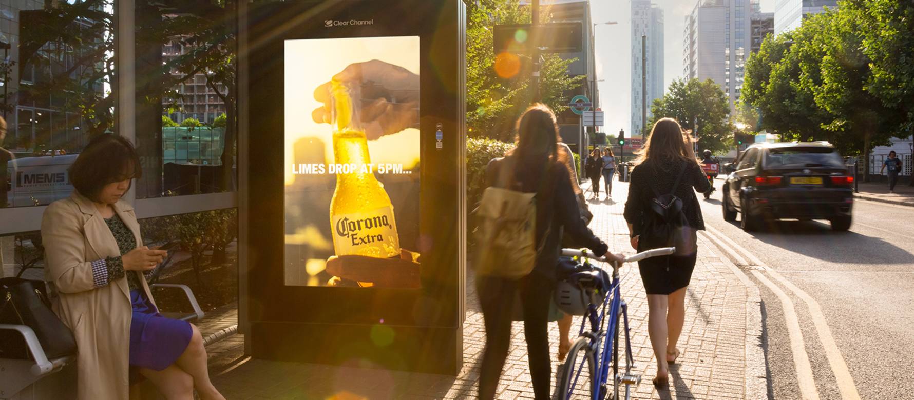 Digital Adshel Live screen featuring Corona advert with cyclist passing by