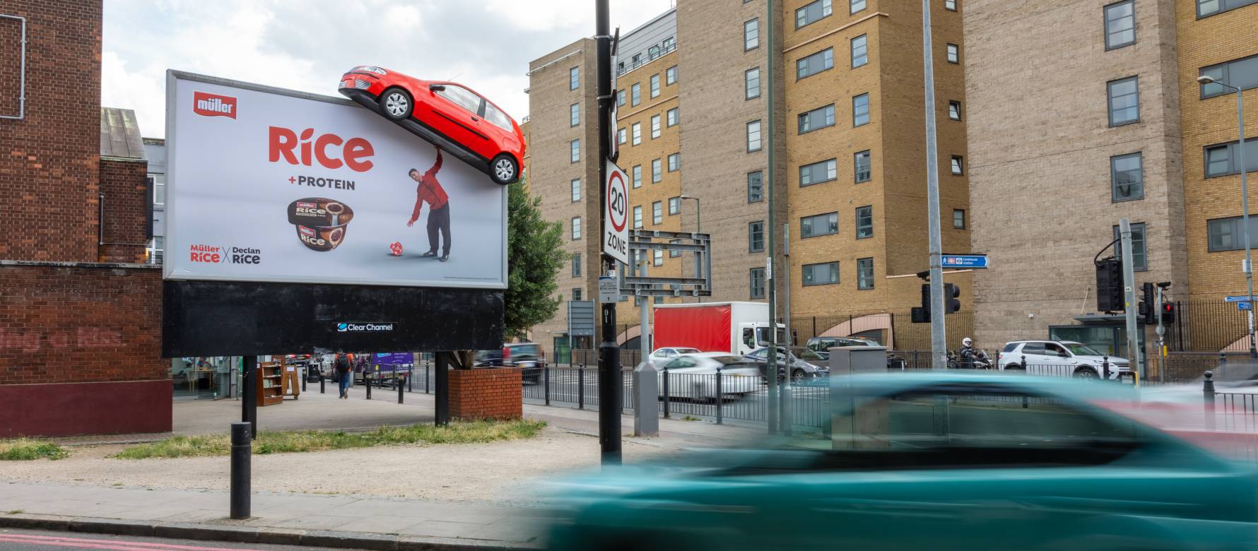 vehicles drive by a billboard showing Muller's campaign of footballer Declan Rice lifting a fake 3D car