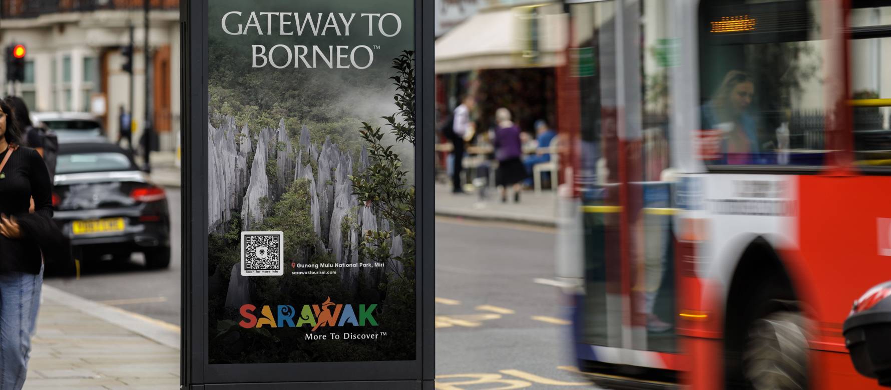 Sarawak advertising on the side of a payphone during the day as a bus passes by