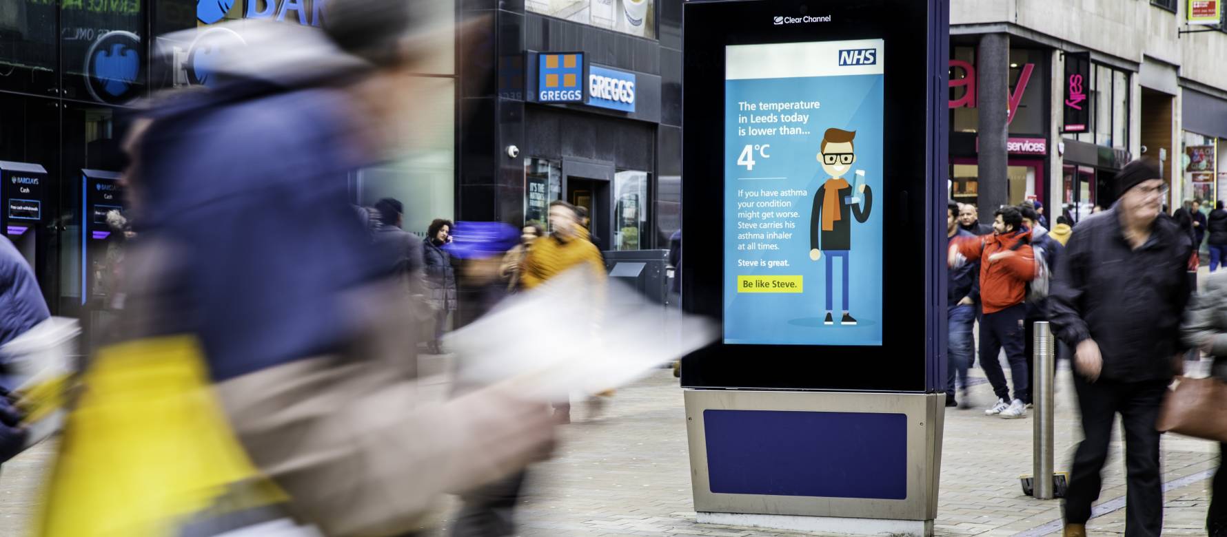 Clear Channel Adshel Live screen showing NHS temperature-triggered digital advertising campaign on a busy high street