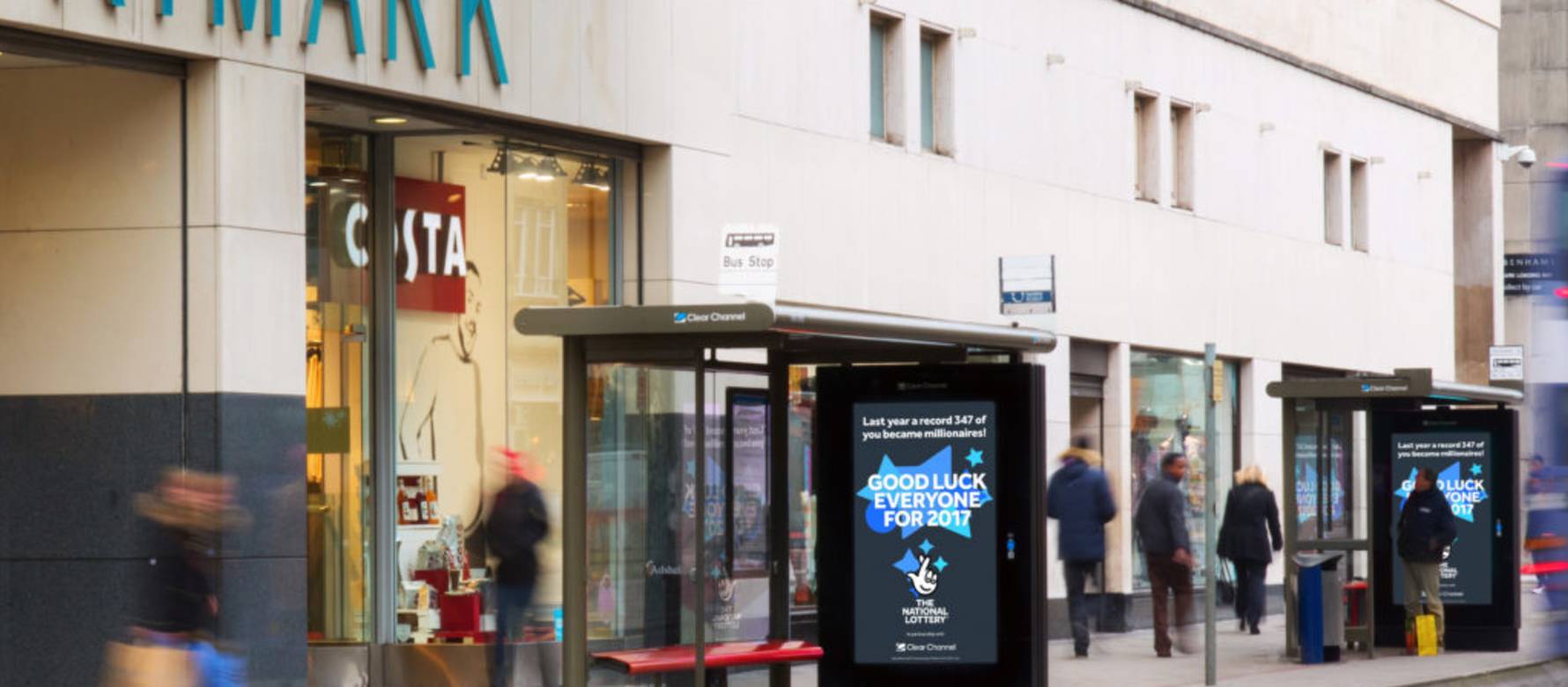 National Lottery advertisement at a bus shelter by a Primark as people walk by during the day