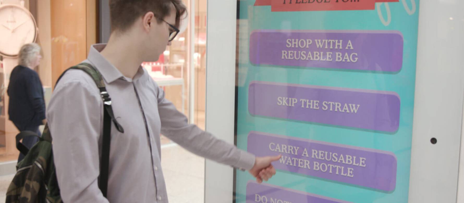 Man in shopping mall using digital screen showing Dumb Ways to Kill Oceans interactive campaign