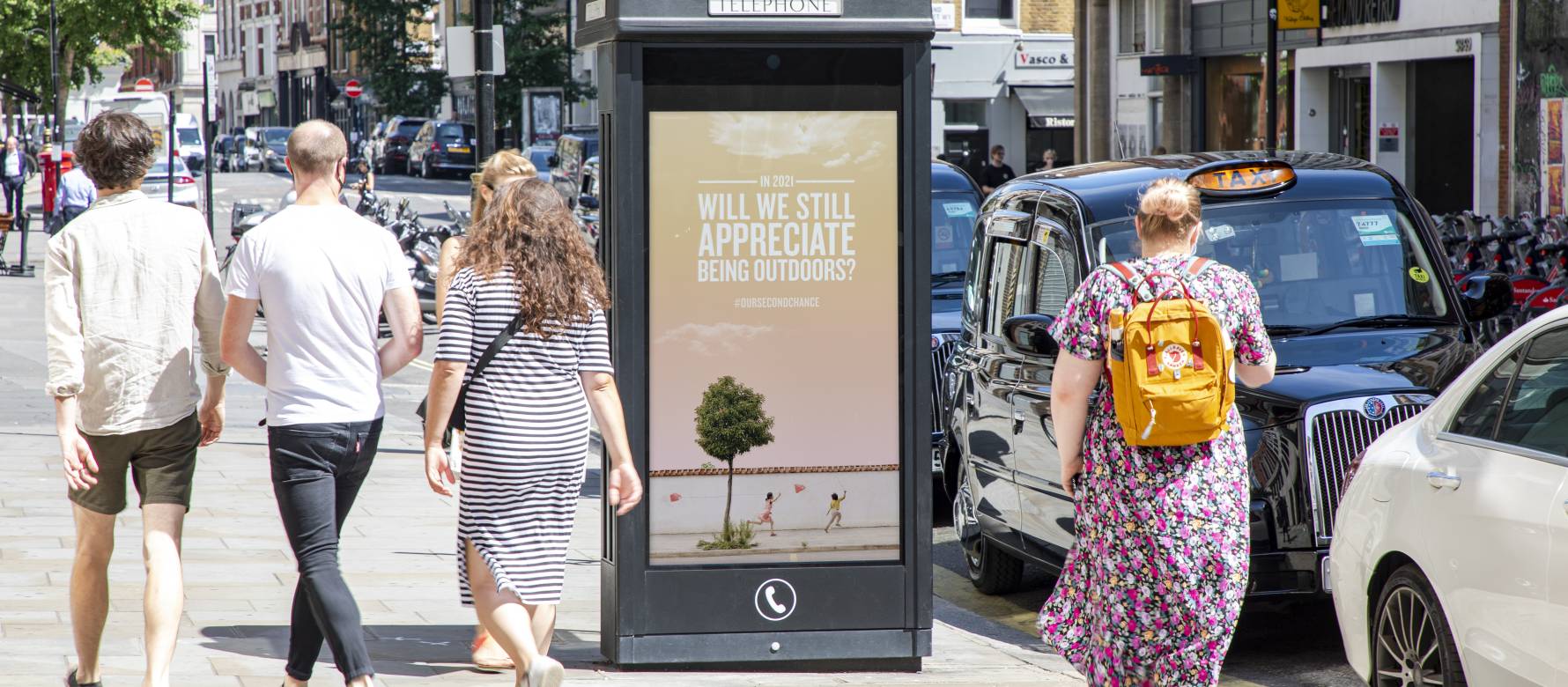 Digital phone box screen on a busy high street showing Our Second Chance Campaign