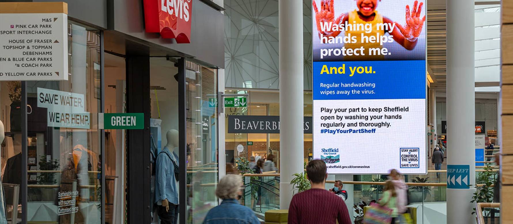 Digital screen in shopping mall outside Levi's store showing NHS advert