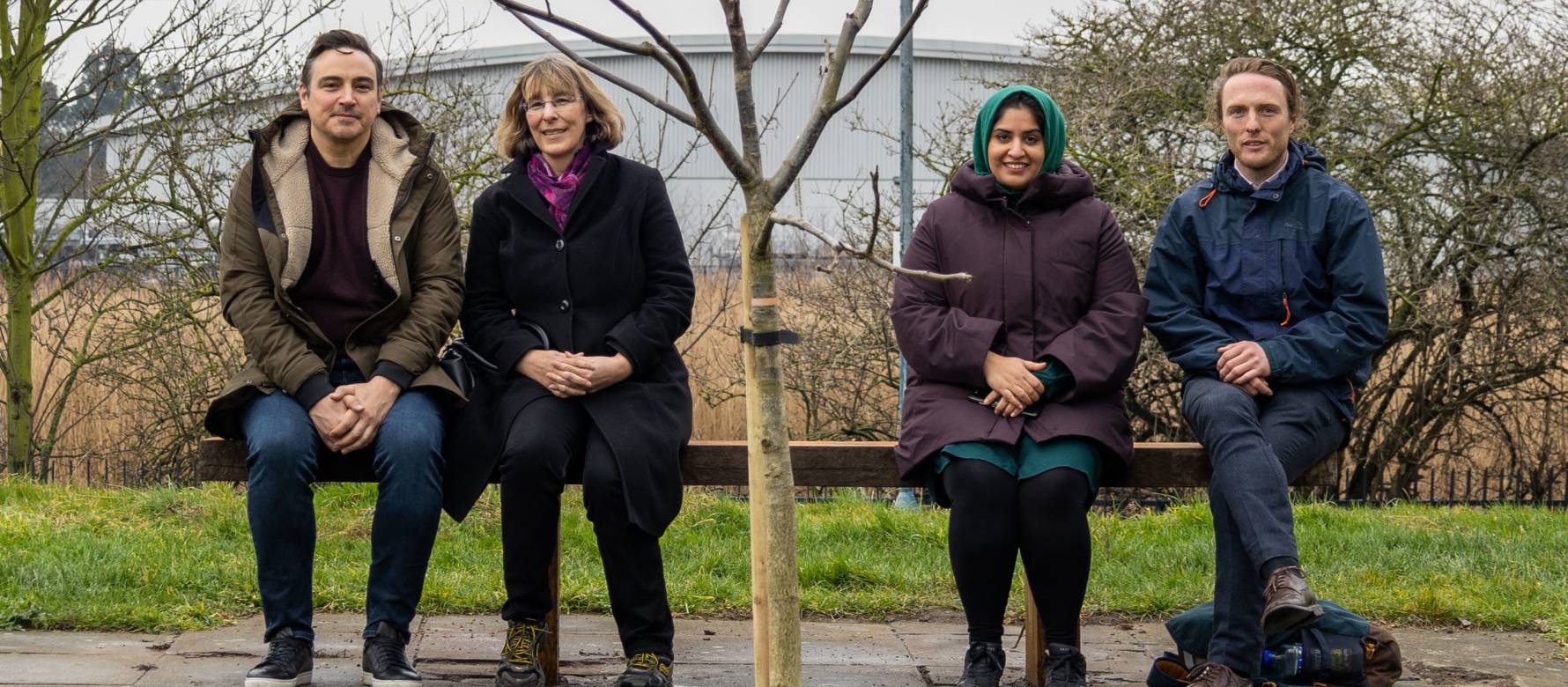 Four people sitting on a bench next to a newly planted tree funded by Clear Channel's re-greening and rejuvenation project