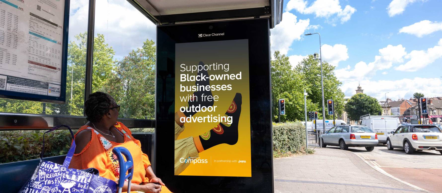 A woman waiting at a bus shelter looking at a Compass advertisement featured on the side of the shelter