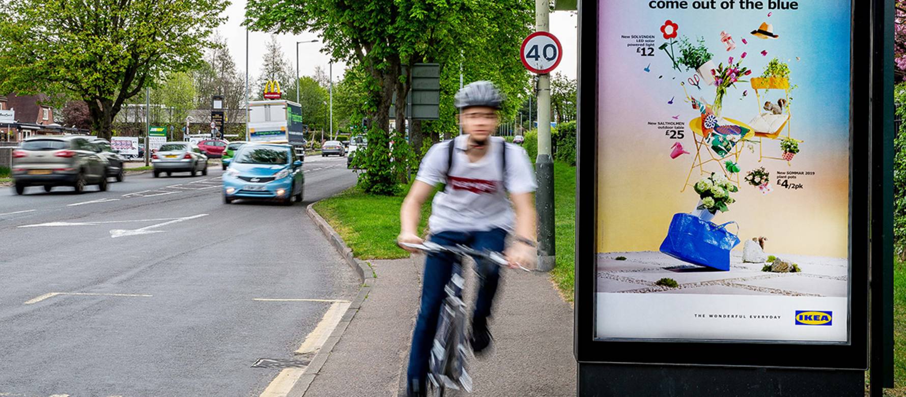 A six-sheet poster on a bus shelter with a cyclist going past
