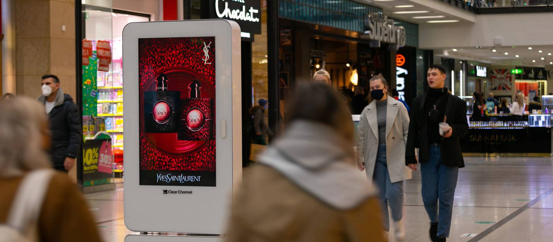 Digital screen in a busy shopping mall showing advert for Yves Saint Laurent Black Opium