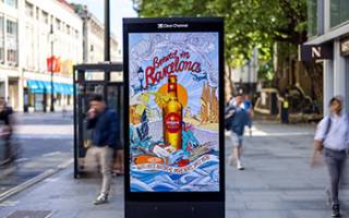 An Estrella beer advert on a digital high street location with people walking by in the daytime