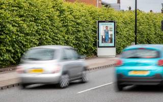 Debenham's light blue with a womans blue dress Adshel advertisement surrounded by 2 cars