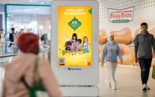 People in a shopping centre walking past a digital poster from Lego
