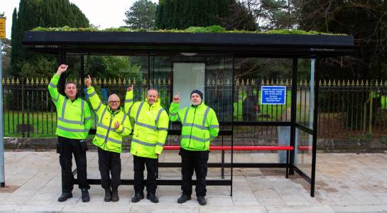 A group of men in reflective jackets standing in front of a  living roof bus stop.