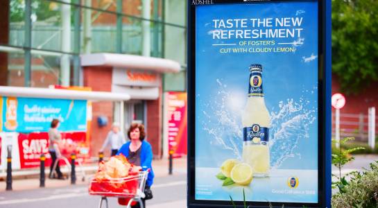 Clear Channel advertising panel outside Sainsburys supermarket with a shopper walking past