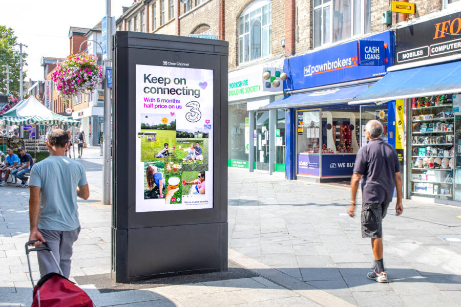 People walking past an Adshel Live display on the sidewalk during the day