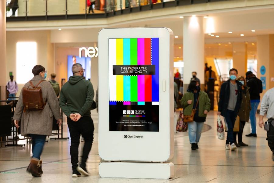 Digital screen in a busy shopping mall showing BBC Creative Diversity campaign