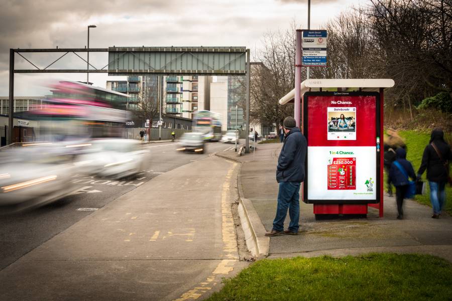 Adshel Classic screen on bus stop on a busy road showing Camelot Lottery advert