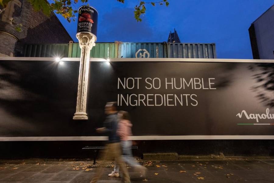 Pedestrians walking by a large Napolina advert which features a giant Corinthian column bursting out of a 96 sheet billboard